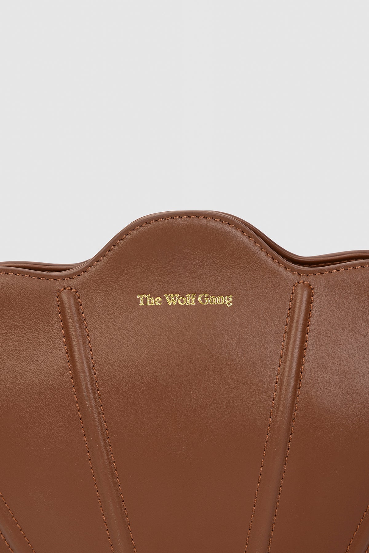 Luxury pebbled leather Suri Bag shell-shaped clutch in Chocolate Brown, with scalloped edge, gold zip, detachable crossbody strap, and ridged detail.