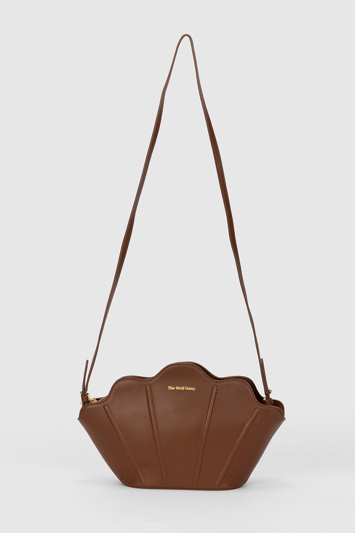 Luxury pebbled leather Suri Bag shell-shaped clutch in Chocolate Brown, with scalloped edge, gold zip, detachable crossbody strap, and ridged detail.