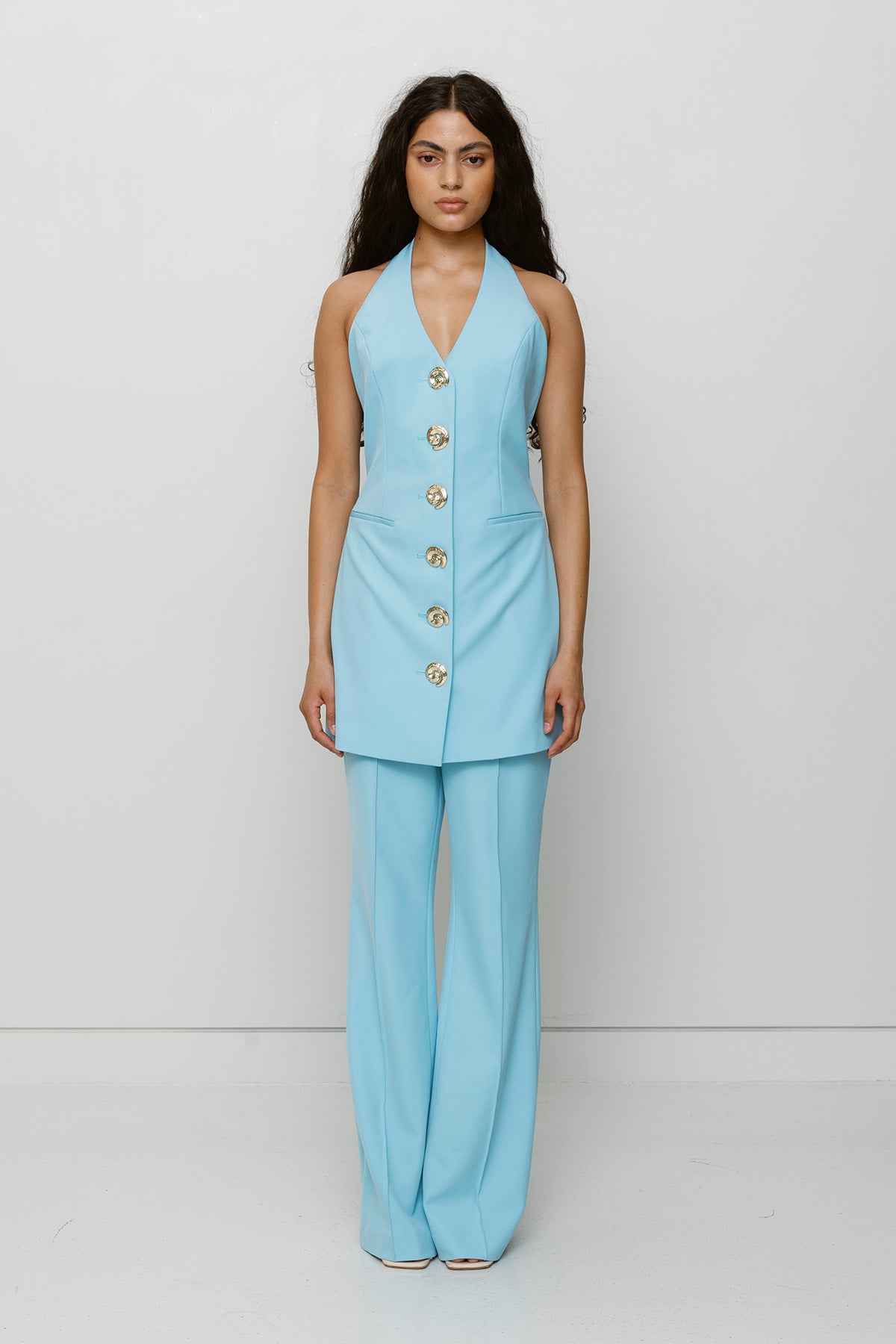 Best-selling women’s Sky Blue Irida mini halter neck vest dress with gold swirl buttons, tie-back, and front welt pocket—wear alone or with matching pants.