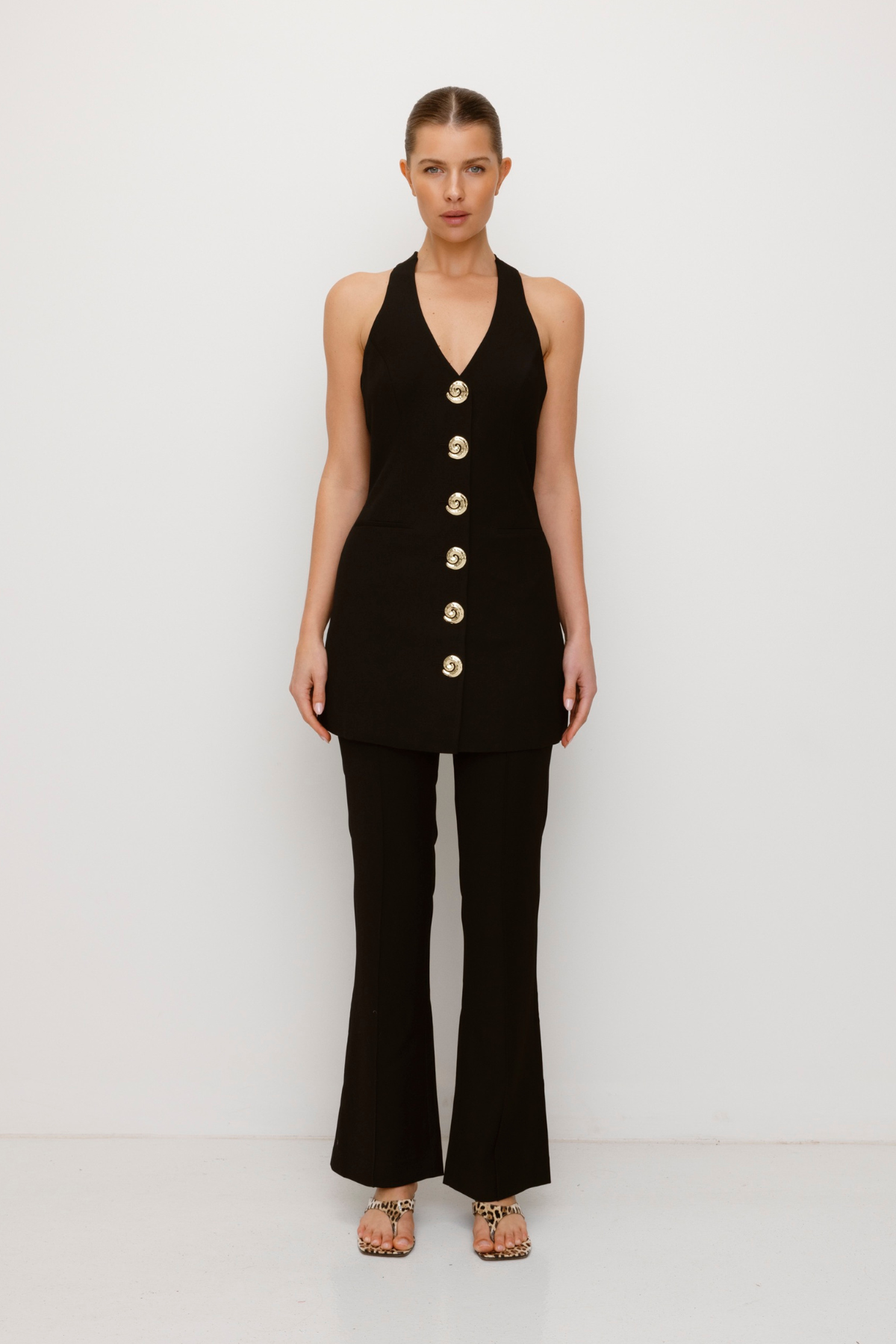 Best-selling women’s Black Irida mini halter neck vest dress with gold swirl buttons, tie-back, and front welt pocket—wear alone or with matching pants.