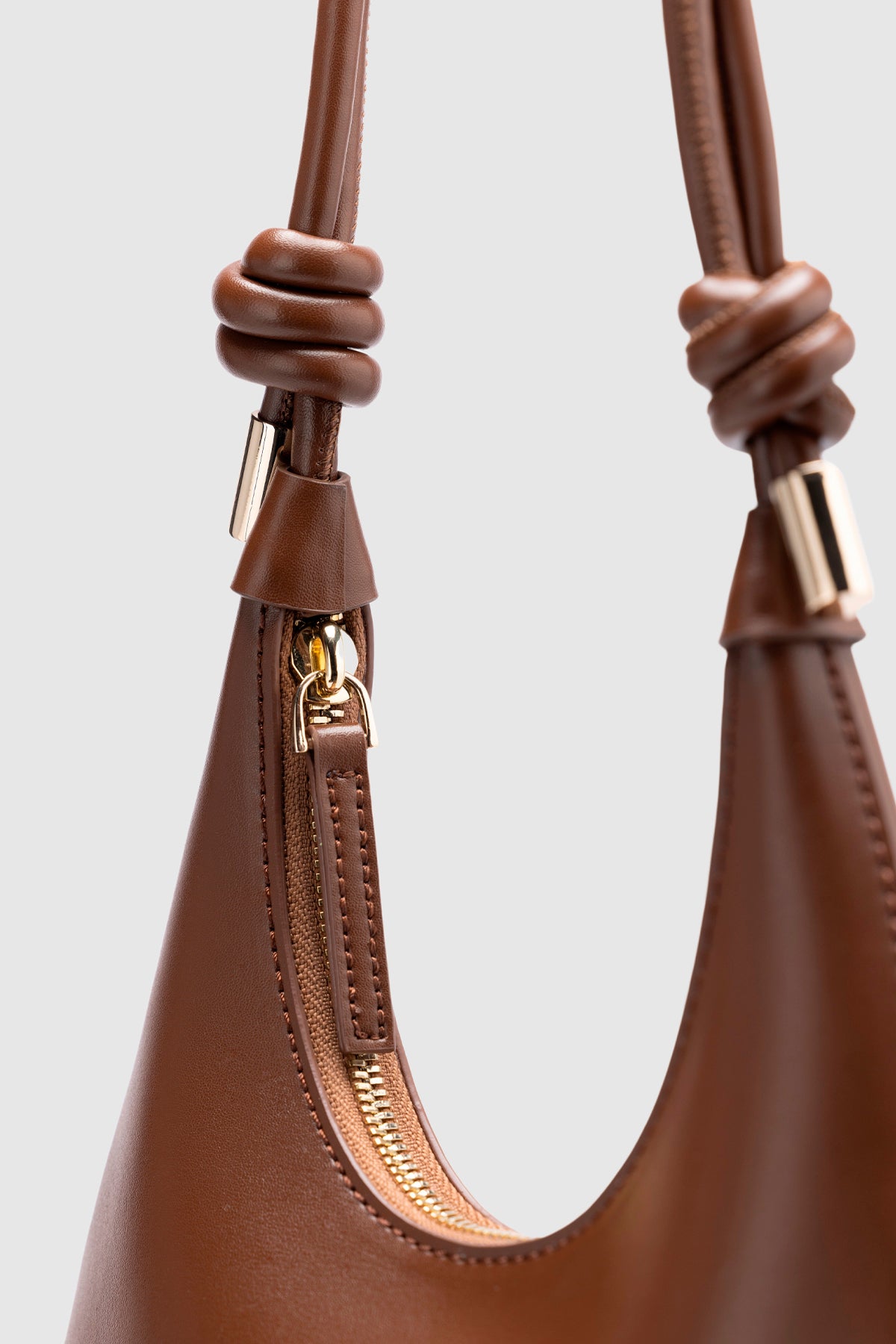 Mini leather crossbody bag with gold rings and adjustable knotted shoulder strap.