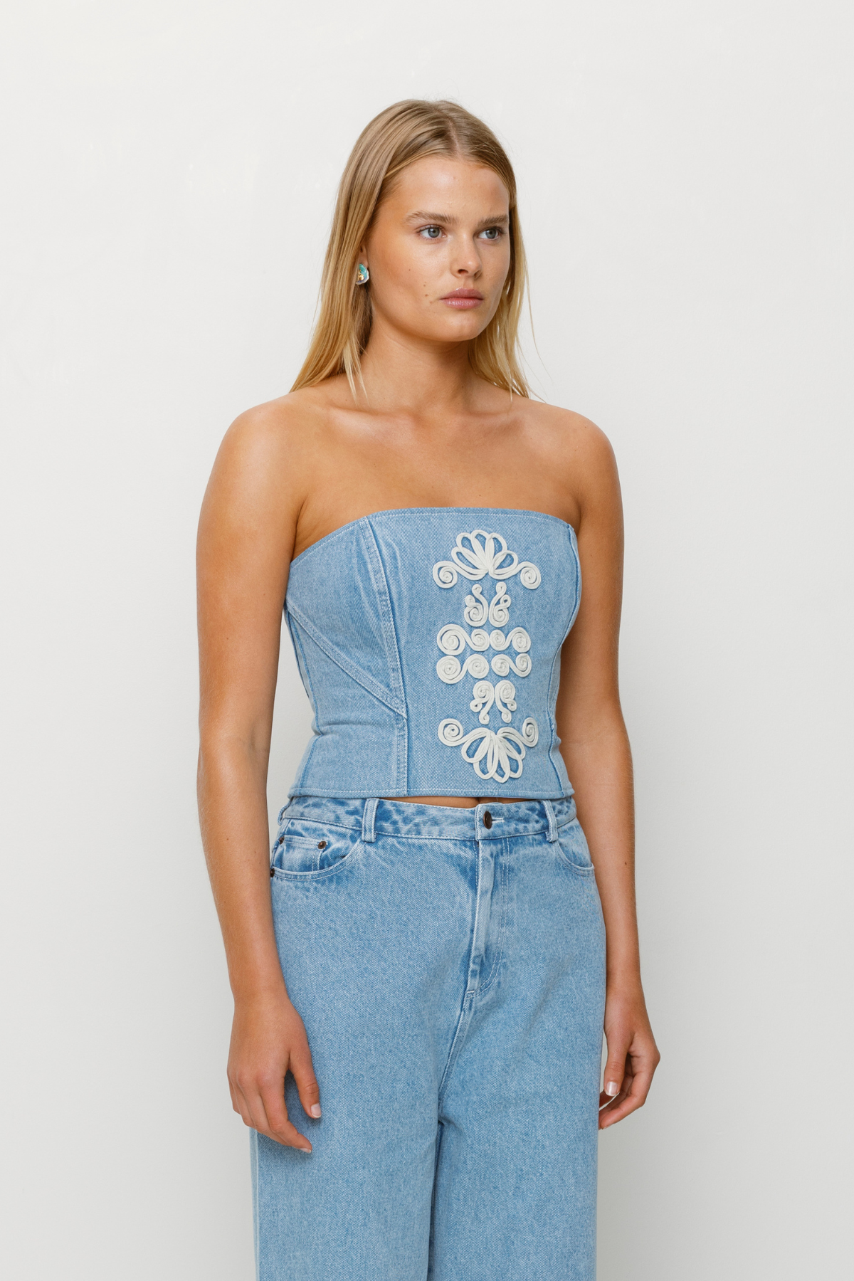 Corset-style denim bustier with boning, functional zip, and custom TWG embroidery by The Wolf Gang, pairs with matching denim jeans.