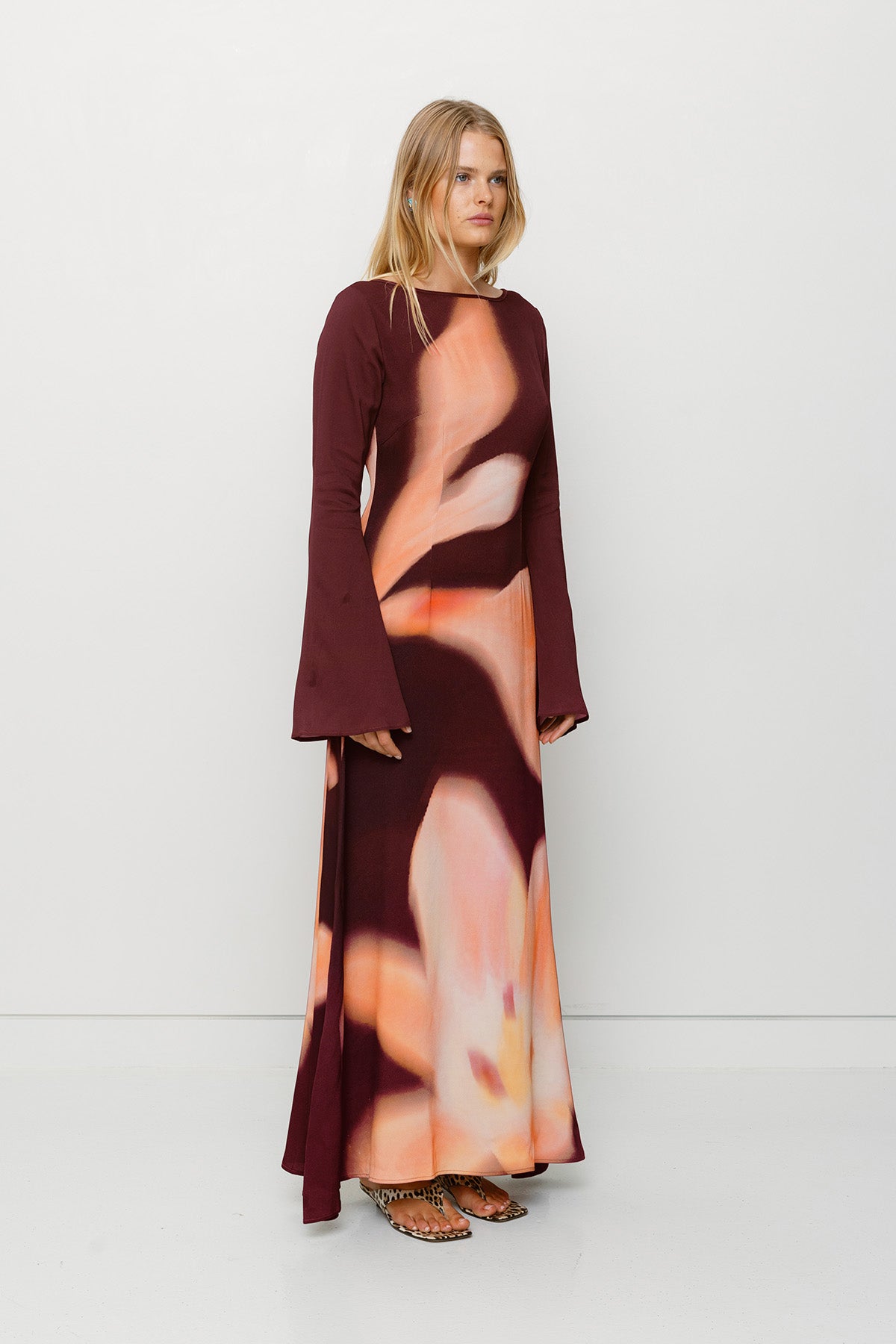 Silky sleeved maxi dress with custom floral TWG print and adjustable back tie, designed for a sleek, glamorous fit.