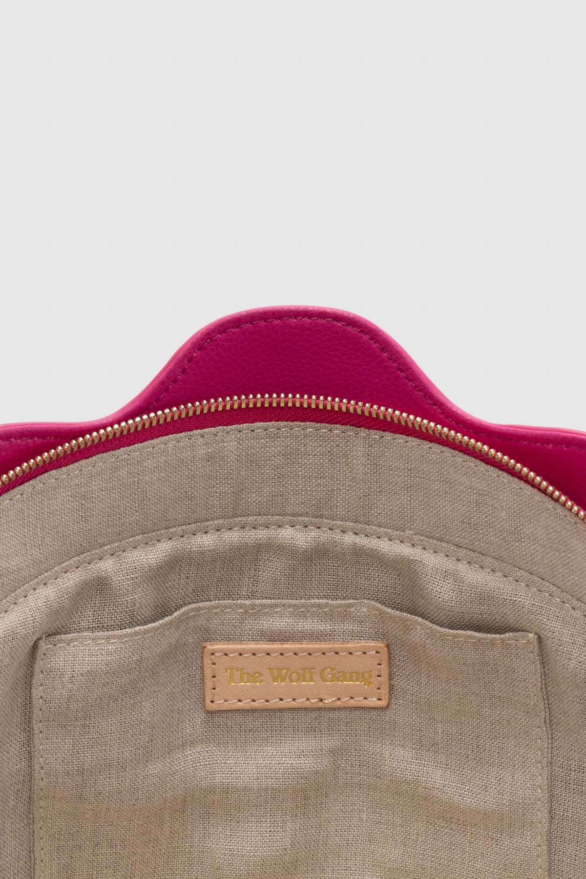Luxury pebbled leather Suri Bag shell-shaped clutch in Flamingo Pink, with scalloped edge, gold zip, detachable crossbody strap, and ridged detail.