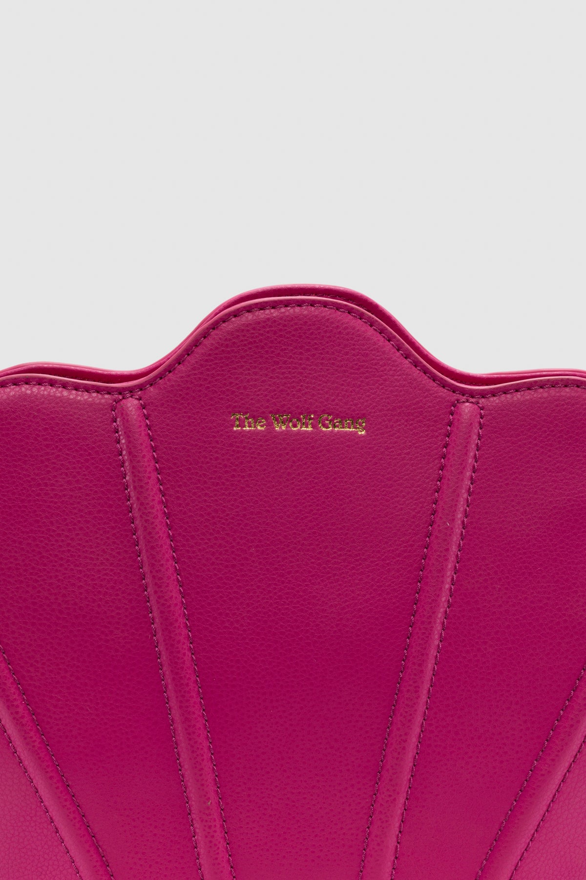 Luxury pebbled leather Suri Bag shell-shaped clutch in Flamingo Pink, with scalloped edge, gold zip, detachable crossbody strap, and ridged detail.