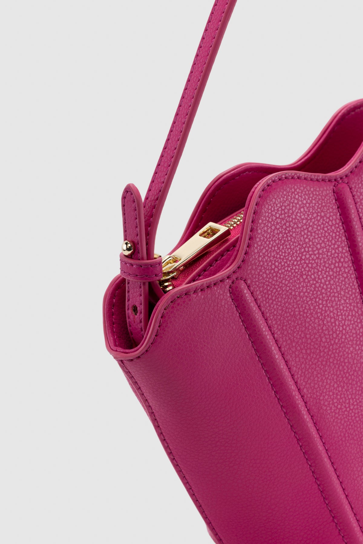 Luxury pebbled leather Suri Bag shell-shaped clutch in Flamingo Pink, with scalloped edge, gold zip, detachable crossbody strap, and ridged detail.