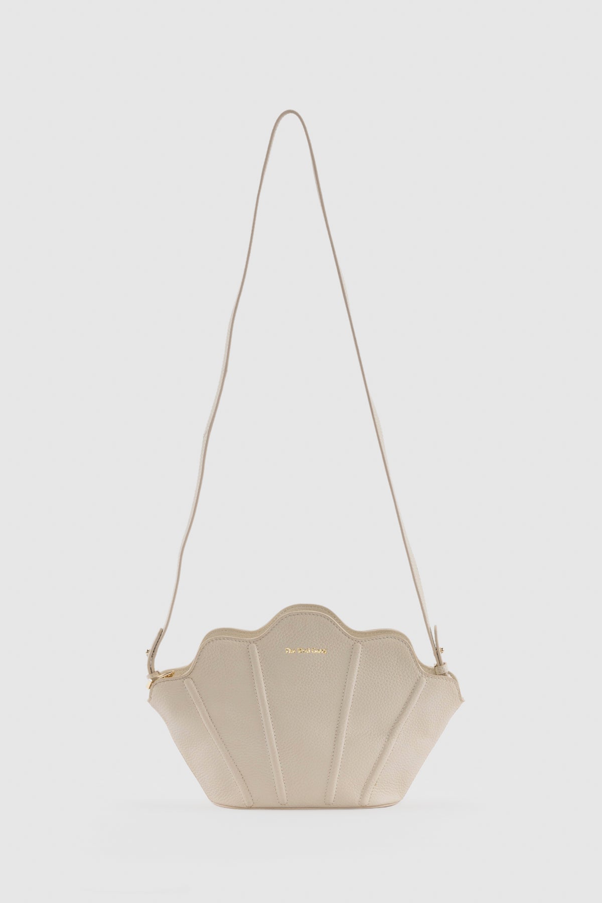 Luxury pebbled leather Suri Bag shell-shaped clutch in Ivory, with scalloped edge, gold zip, detachable crossbody strap, and ridged detail.