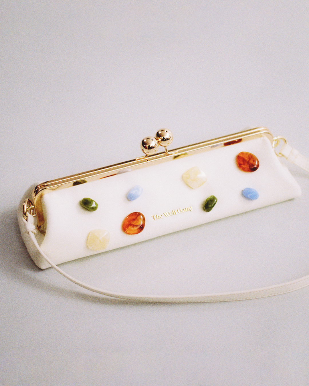 Go to new collection. Pictured: Clutch bag with colorful gemstone decorations on a light gray 
