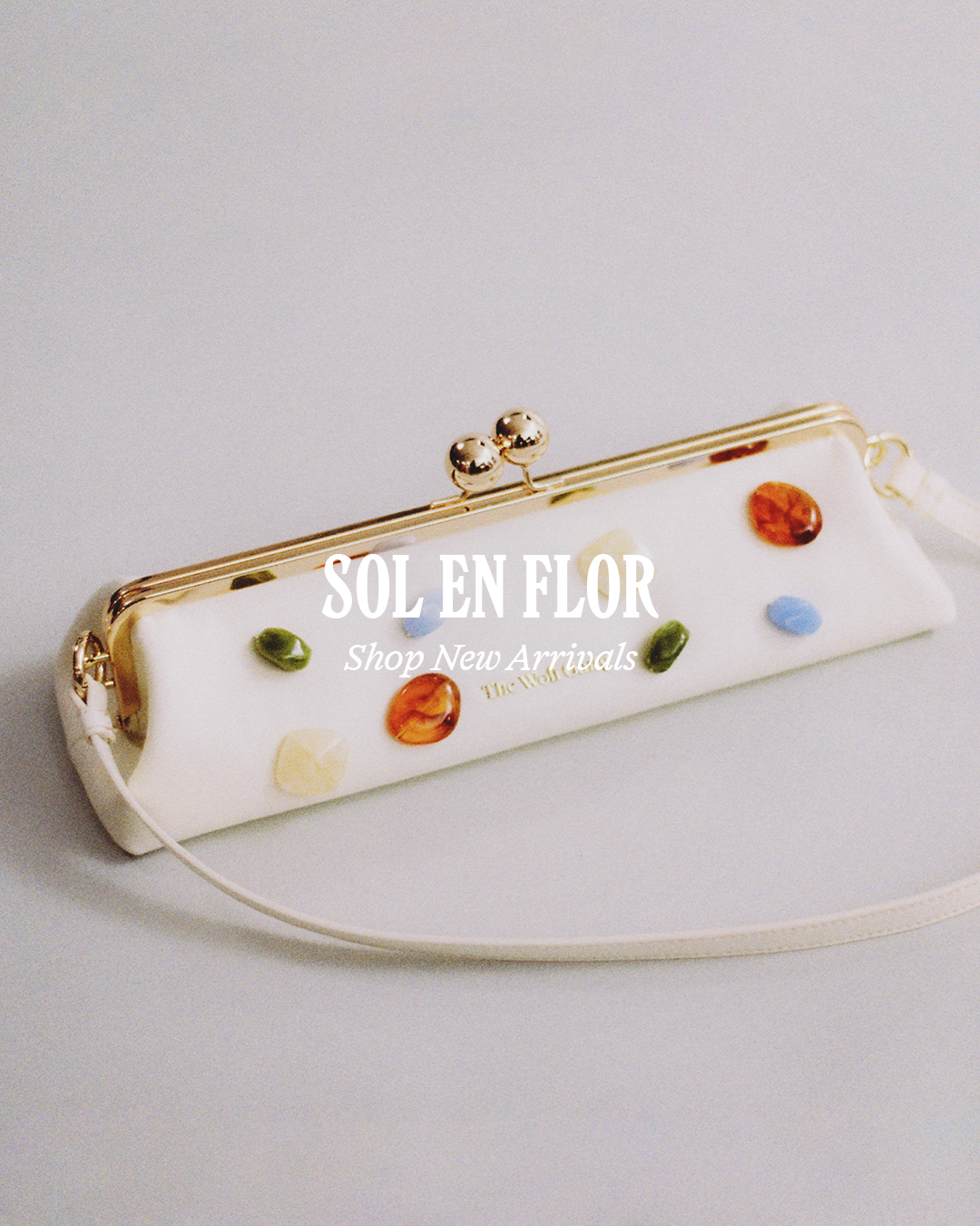 White clutch bag with colourful gemstones on a light grey background.