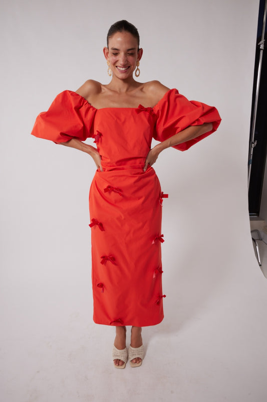 Mid-length off-shoulder dress with elasticated puff sleeves and velvet bow detail by The Wolf Gang, in pink, red, and black.